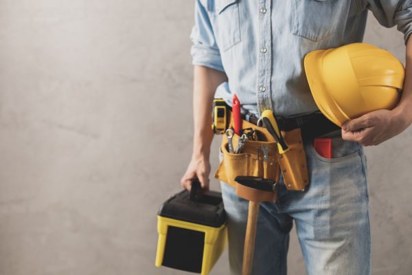 Worker man holding construction helmet and toolbox near wall. Ma Worker man holding construction helmet and toolbox near wall. Male hand and tools for house room renovation. Home renovation concept